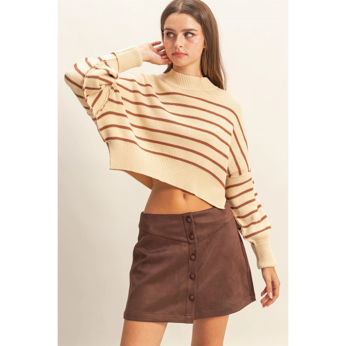 Woman wearing a beige and brown striped crop sweater with a mock neck.