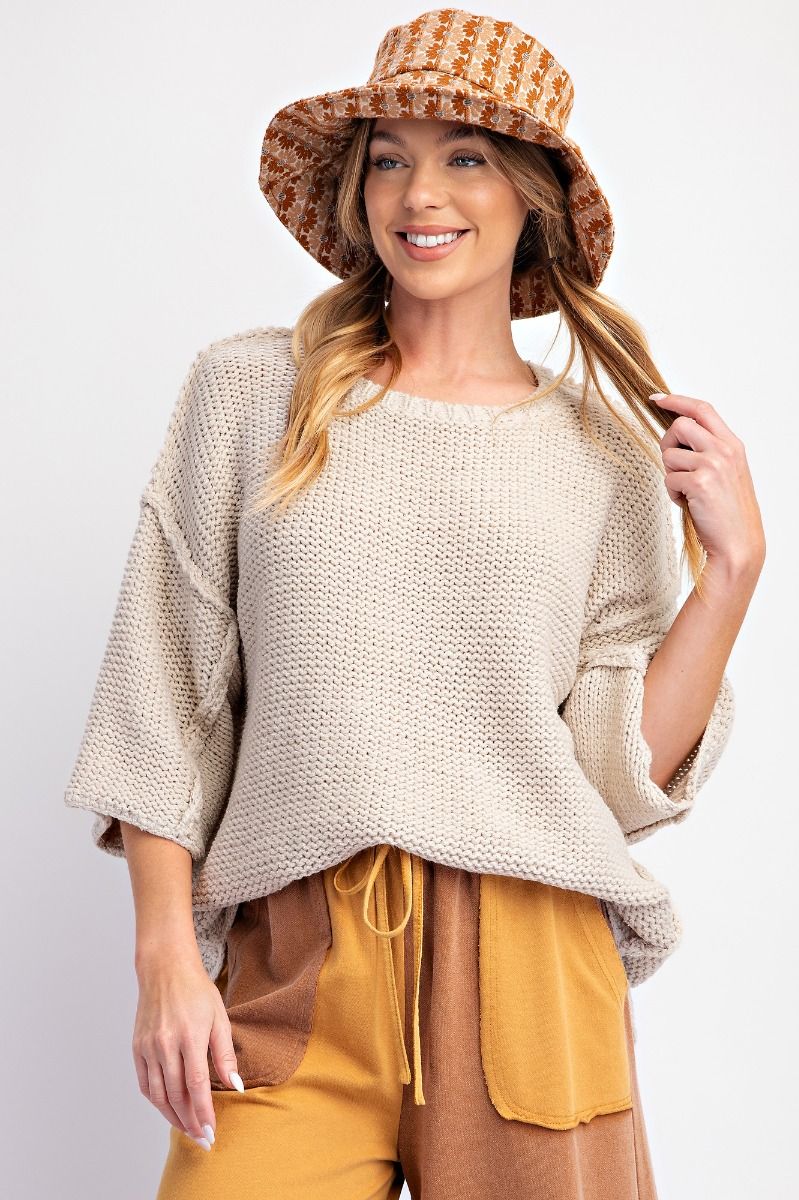 Woman wearing a beige knit sweater with dolman 3/4 length sleeves and exposed reverse seams.