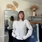 Model wearing an ivory sweater with intricate stitching and puffed sleeves.
