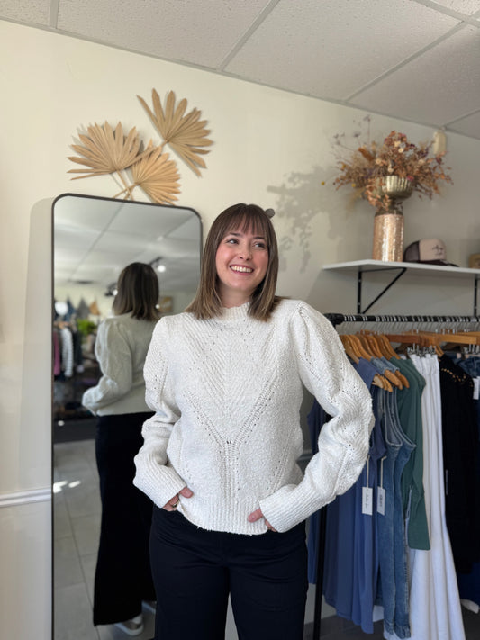 Model wearing an ivory sweater with intricate stitching and puffed sleeves.