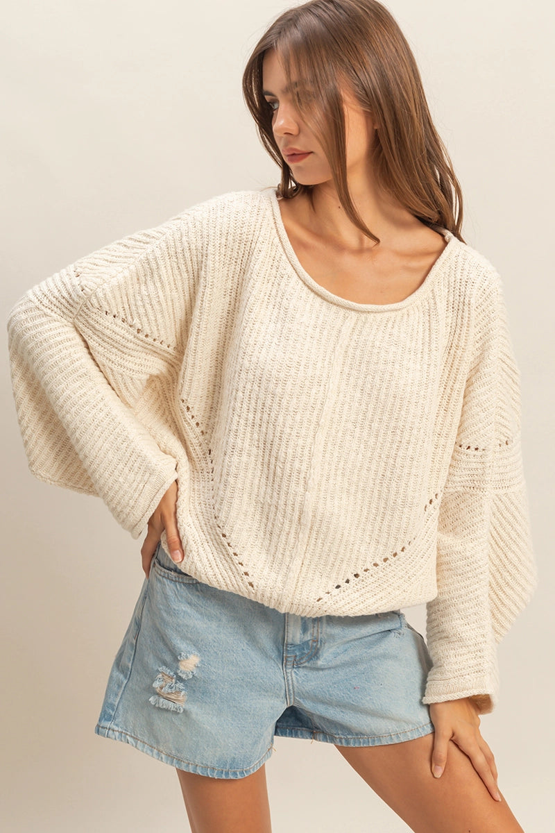 Woman wearing a cream sweater with rib detailing and a drop shoulder oversized fit.