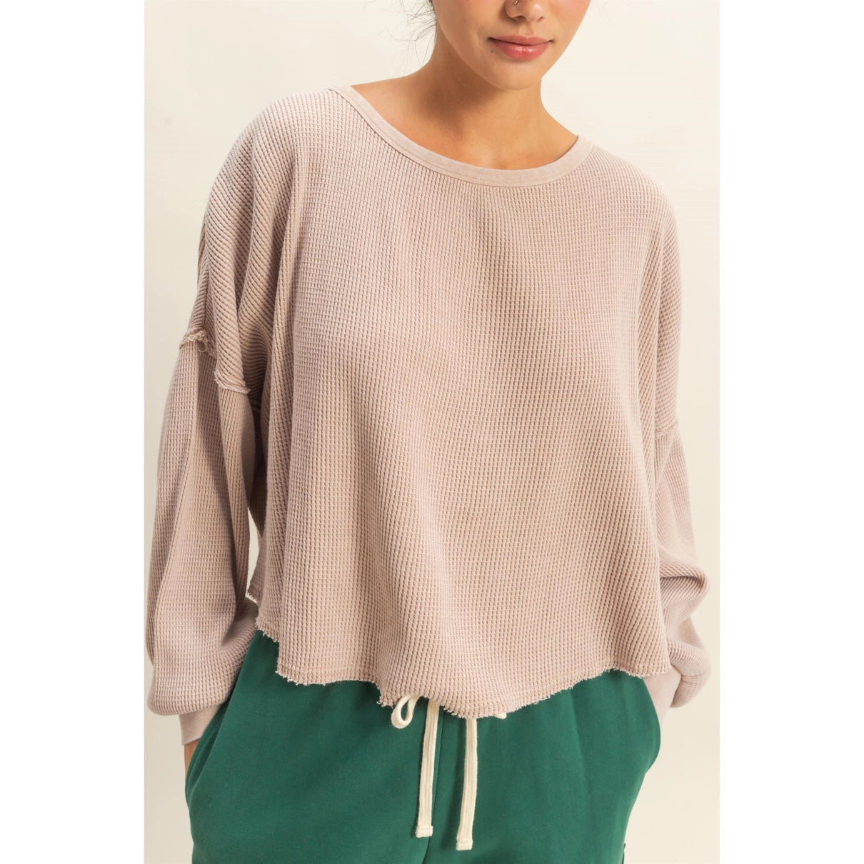 Woman wearing a light taupe waffle knit top with raw edges.