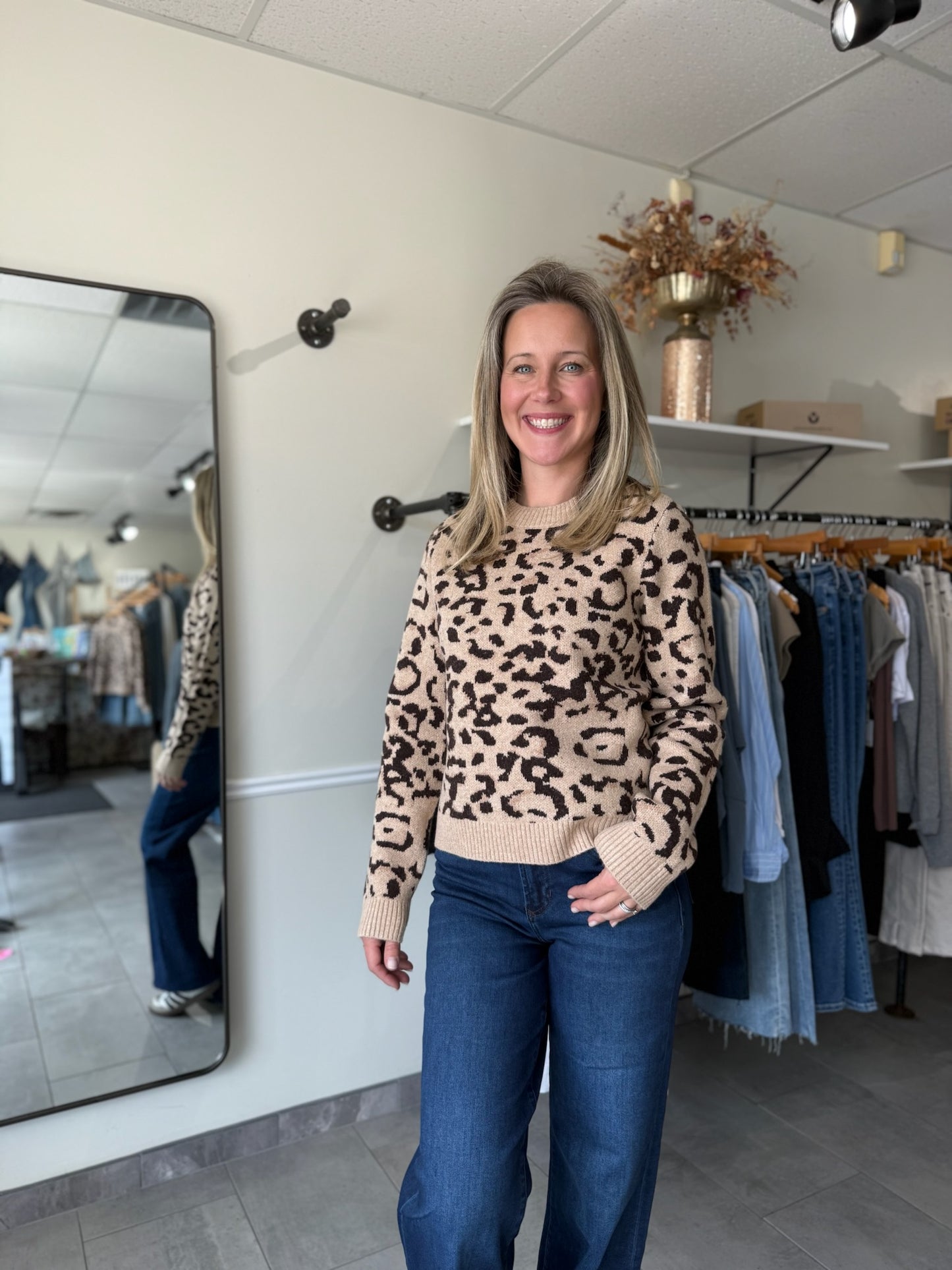 Woman wearing a leopard print sweater and blue jeans in a clothing store.