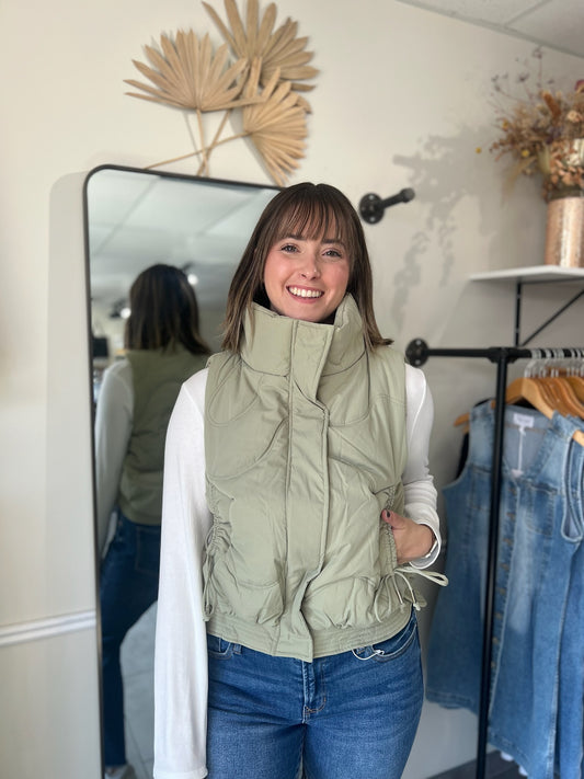 Model wearing green puffer vest with quilting details and side ties. 