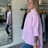 woman wearing a light pink oversized tunic sweater paired with denim.