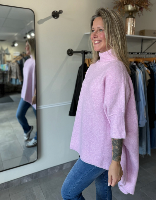 woman wearing a light pink oversized tunic sweater paired with denim.