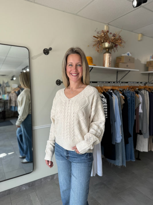 Woman wearing an ivory, cable knit sweater and blue jeans.