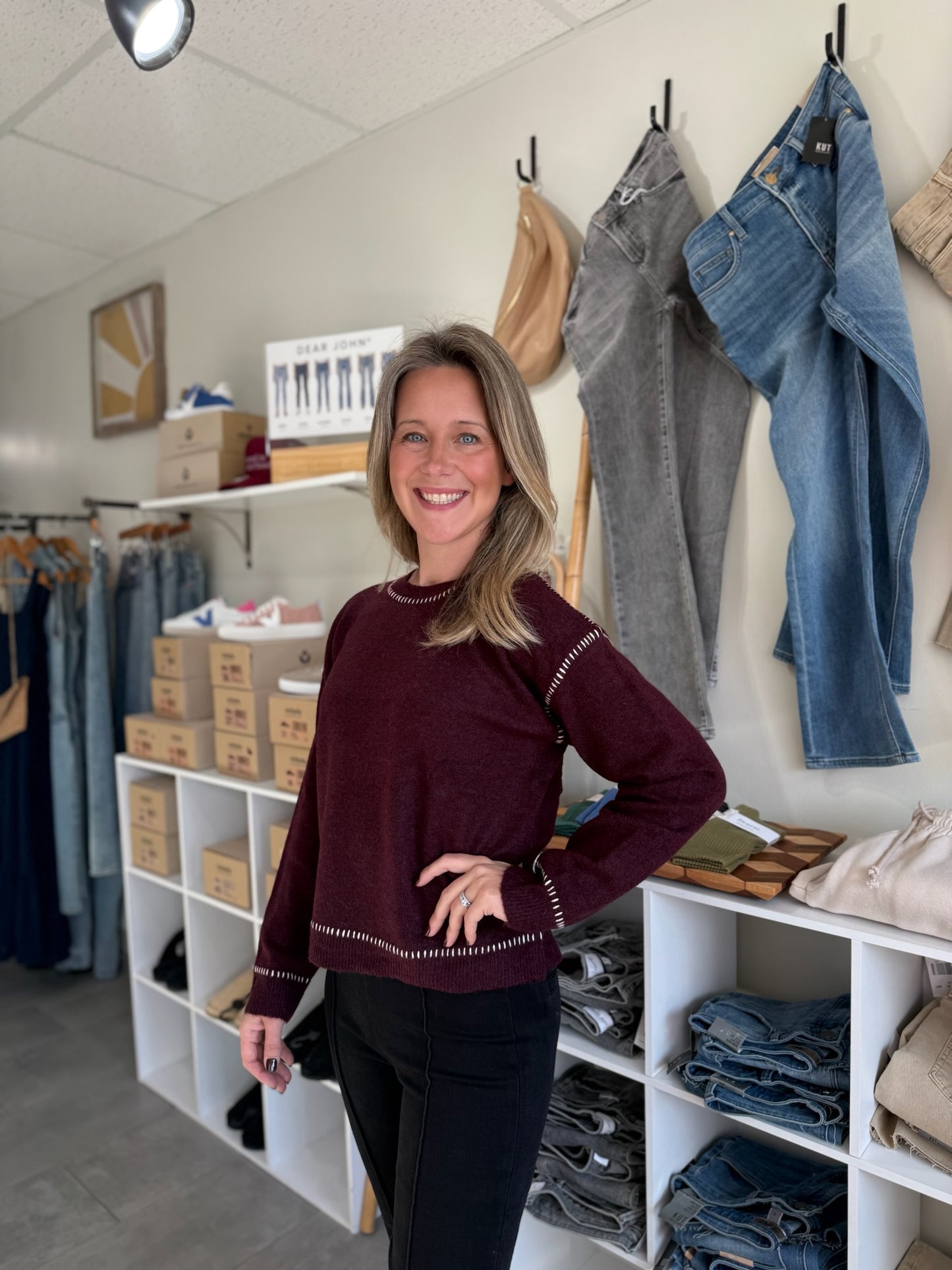 Model wearing bordeaux colored sweater with white stitching.