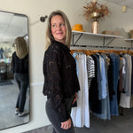 Woman in a black top with eyelet details and black jeans standing in a clothing store.