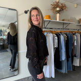 Woman in a black top with eyelet details and black jeans standing in a clothing store.