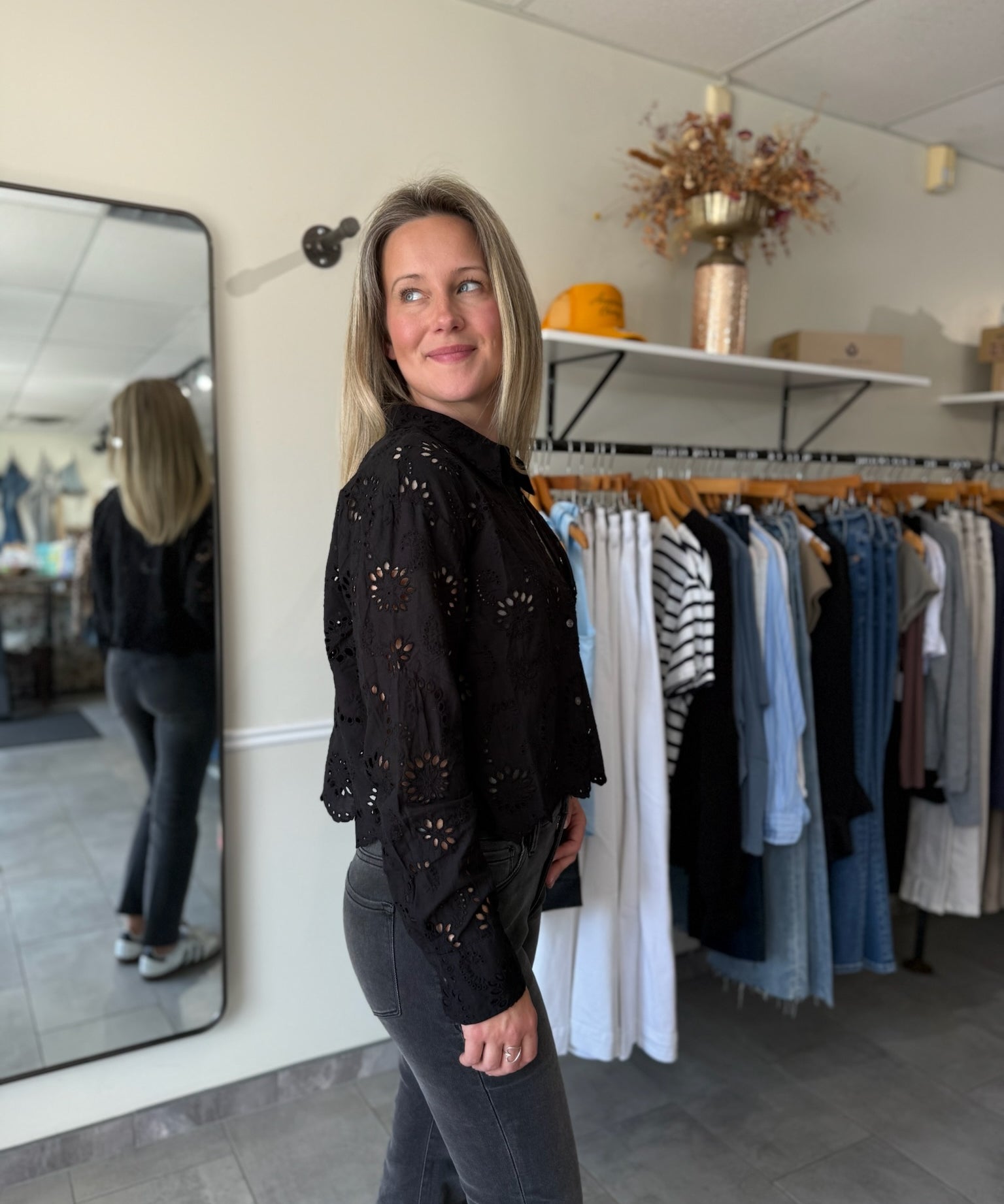 Woman in a black top with eyelet details and black jeans standing in a clothing store.