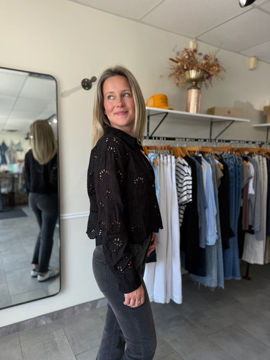 Woman in a black top with eyelet details and black jeans standing in a clothing store.