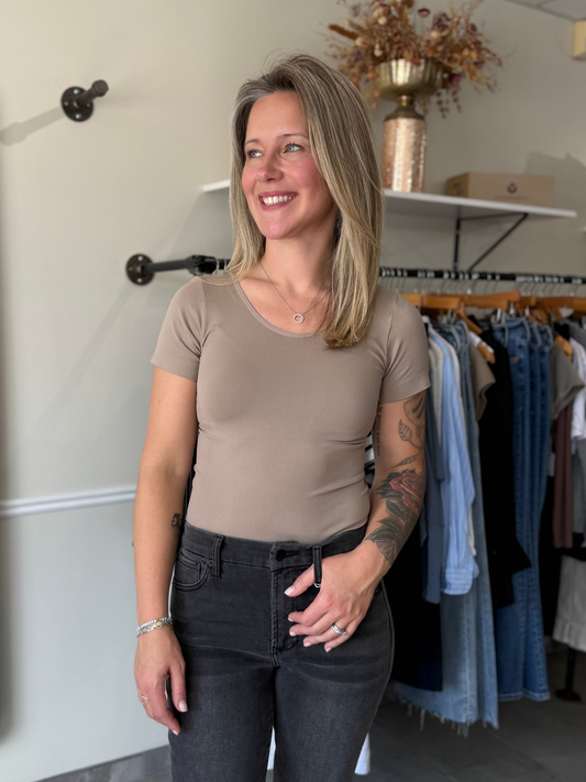 Woman wearing a fitted, beige, seamless t-shirt paired with black denim.