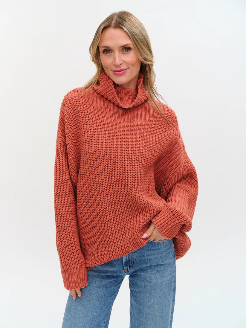 Woman wearing a rust-colored knitted sweater with turtle neck and oversized fit from Six Fifty.